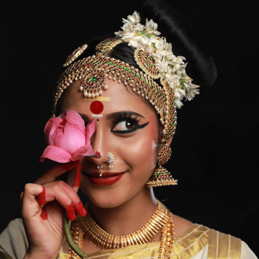 1. A woman in traditional Indian attire gracefully holds a flower, embodying the elegance of Mohiniyattam dance.<br />