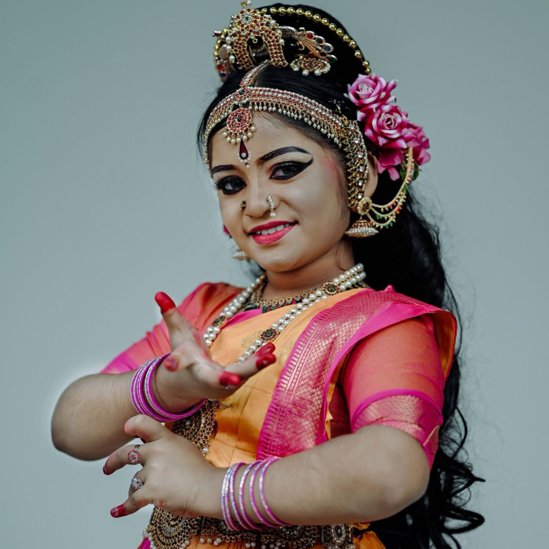 2. A woman dressed in traditional Indian clothing, holding a flower, representing the art of Bharatanatyam.</p>
<p>