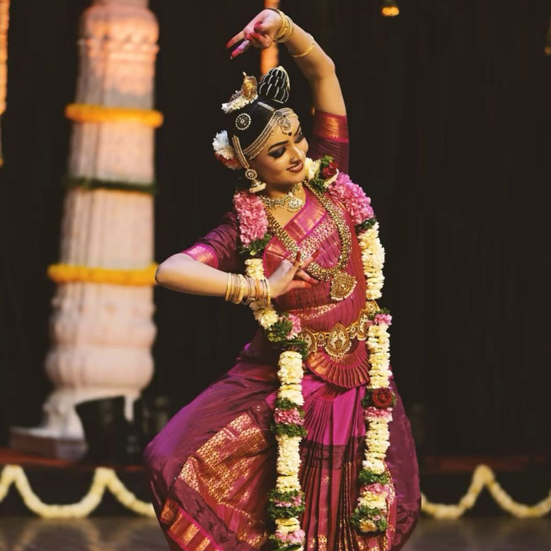 .3. A woman in traditional Indian dress stands elegantly, holding a flower, showcasing the art of Kuchipudi dance.</p>
<p>